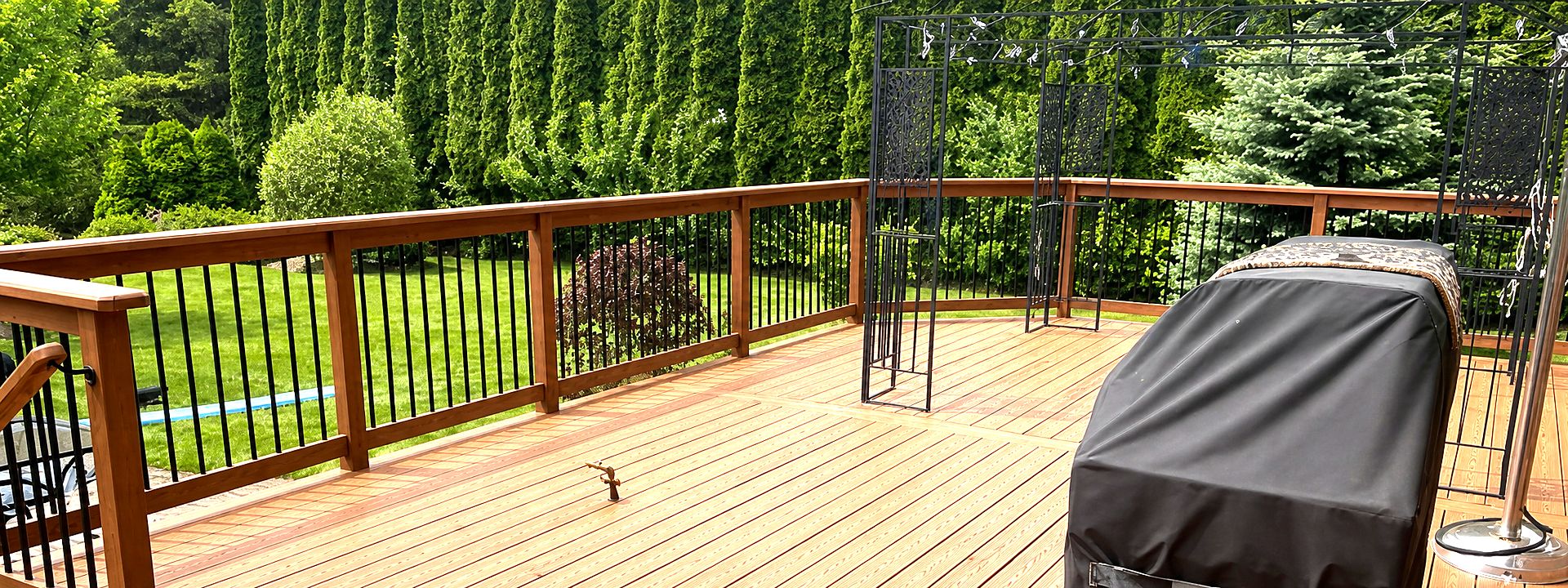 Freshly stained warm-toned deck with wood railing overlooking a cedar hedge and lawn