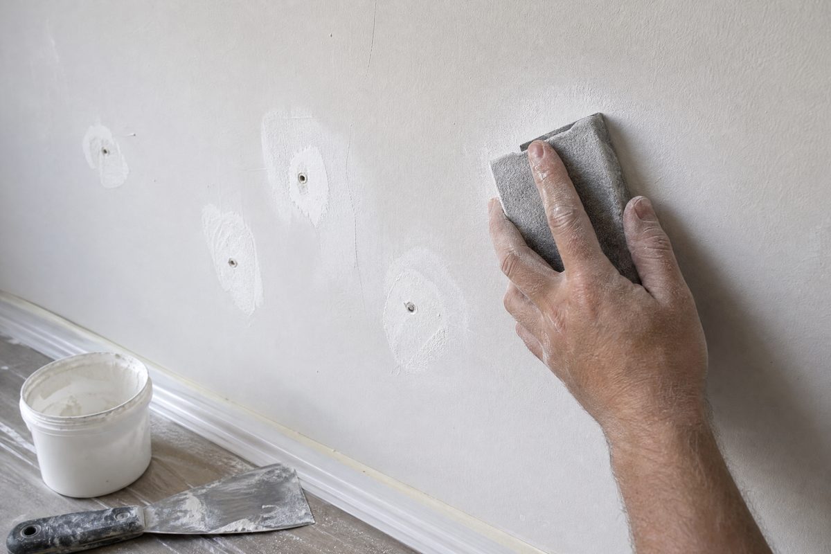 Filled and sanded wall anchor holes on interior drywall being smoothed with a sanding block before painting