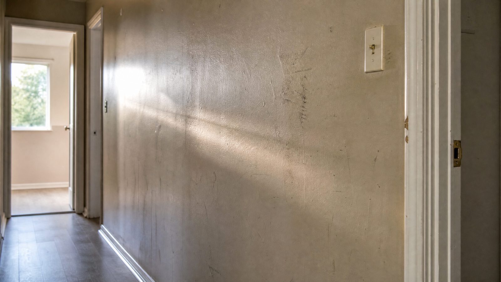 Worn interior hallway wall in a Barrie home showing scuff marks and burnished patches revealed by raking sunlight