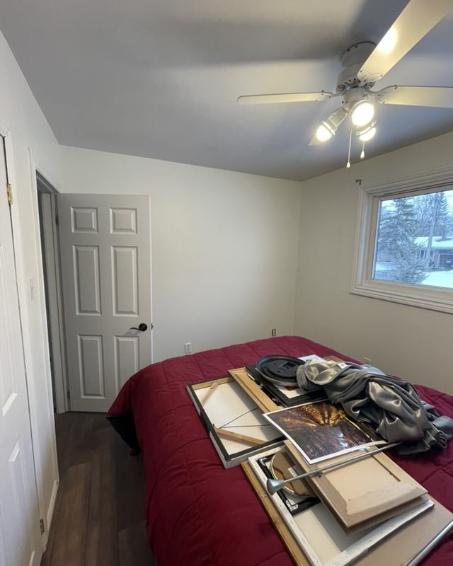 Bedroom after painting with fresh walls, white door and casing, framed artwork stacked on the bed ready to be rehung