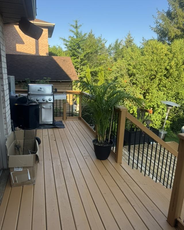 Deck finished in a dark brown stain with black metal railing, gas barbecue and potted plants on the boards