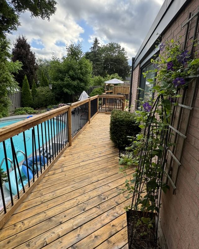 Long stained deck walkway running beside an above-ground pool, planters and climbing vines along the railing