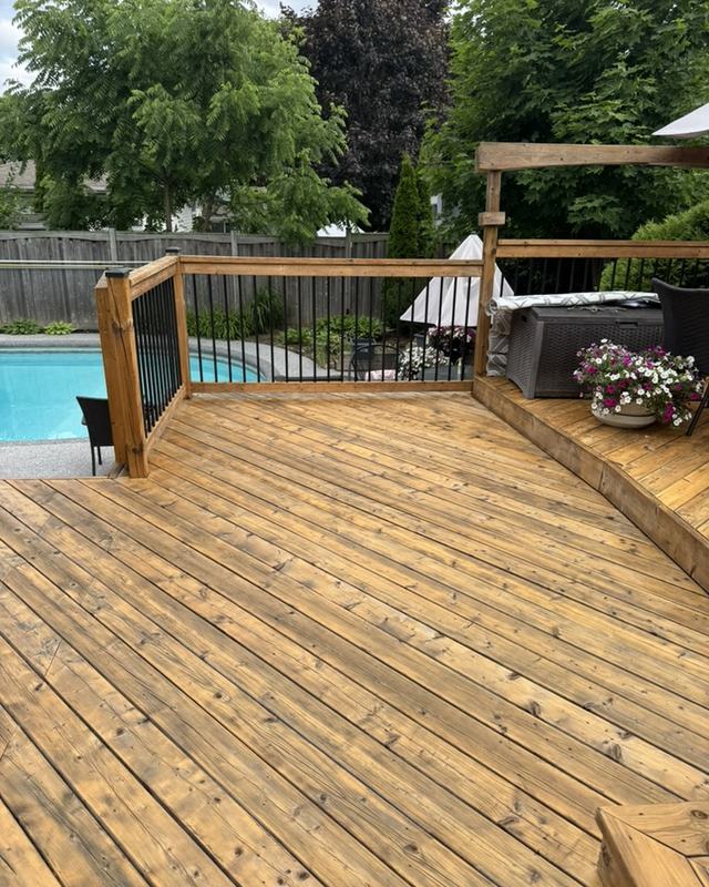 Large stained wraparound pool deck in a natural cedar tone with pergola, patio furniture and privacy fence