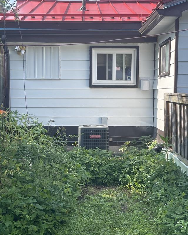 Side elevation of a white-sided home with a red metal roof after exterior painting, window trim cut in clean
