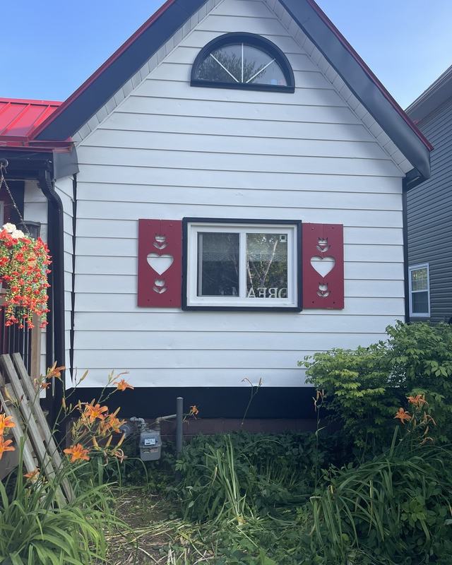 Gable end of a white-sided home after exterior painting with red decorative shutters and a fan window