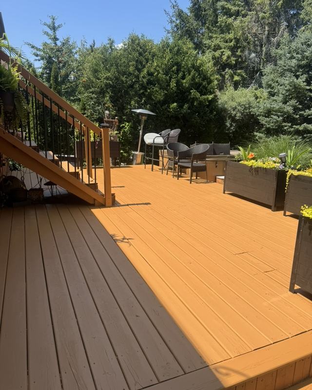 Freshly restained deck in a warm cedar tone with wood railing, planter boxes and a treeline behind