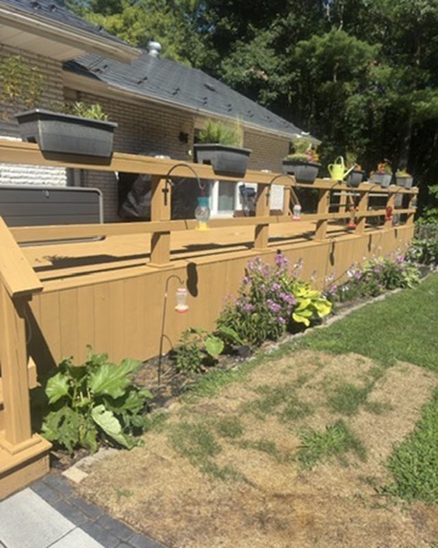 Stained deck railing with built-in planter boxes full of flowers, lawn and garden beyond