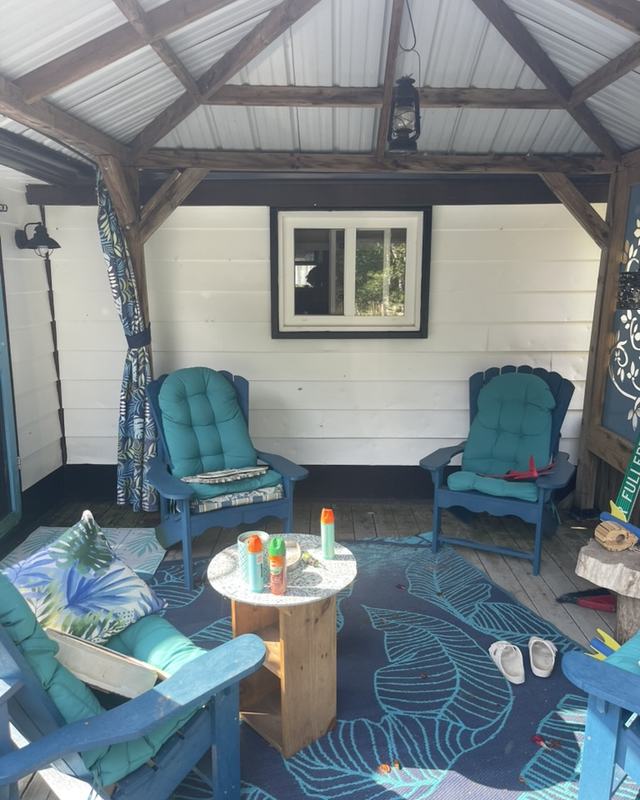 Timber-framed covered porch with walls painted white, teal patio chairs, outdoor rug and hanging curtains