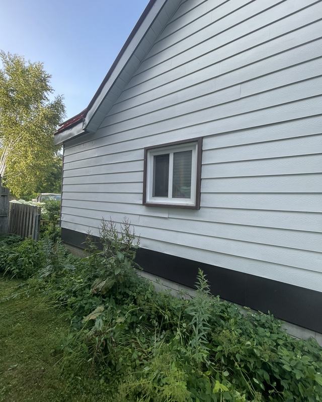 Rear elevation of a white-sided bungalow after exterior painting, basement window trim and soffit finished