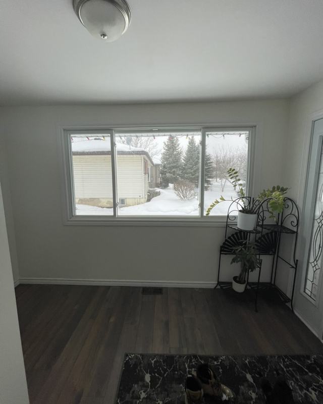 Front room after painting with a large picture window, white walls and trim, dark plank flooring