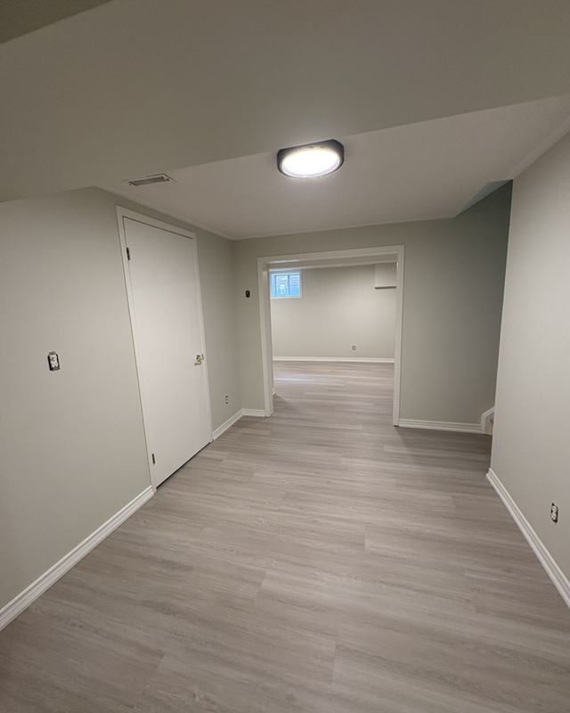 Finished basement hallway painted in a light neutral with white doors and trim over grey plank flooring