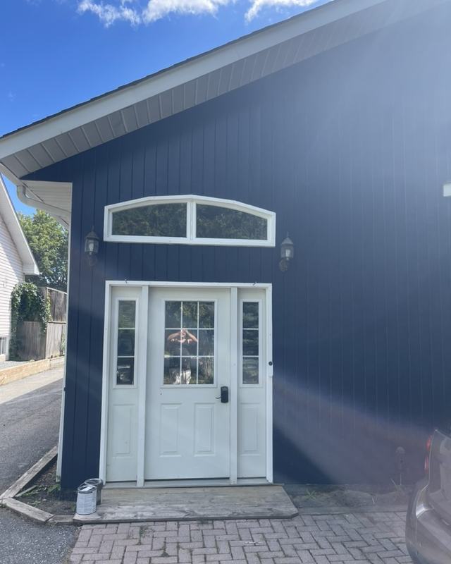 Front entry of a home painted deep navy with a white six-panel door, transom window and paver walkway