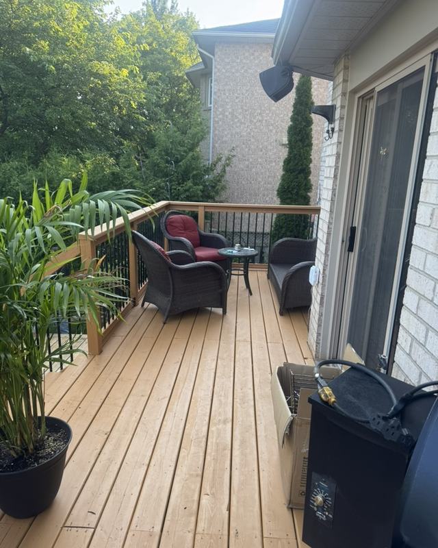Side-yard deck stained in a natural tone with wicker patio chairs, potted palms and a sliding patio door