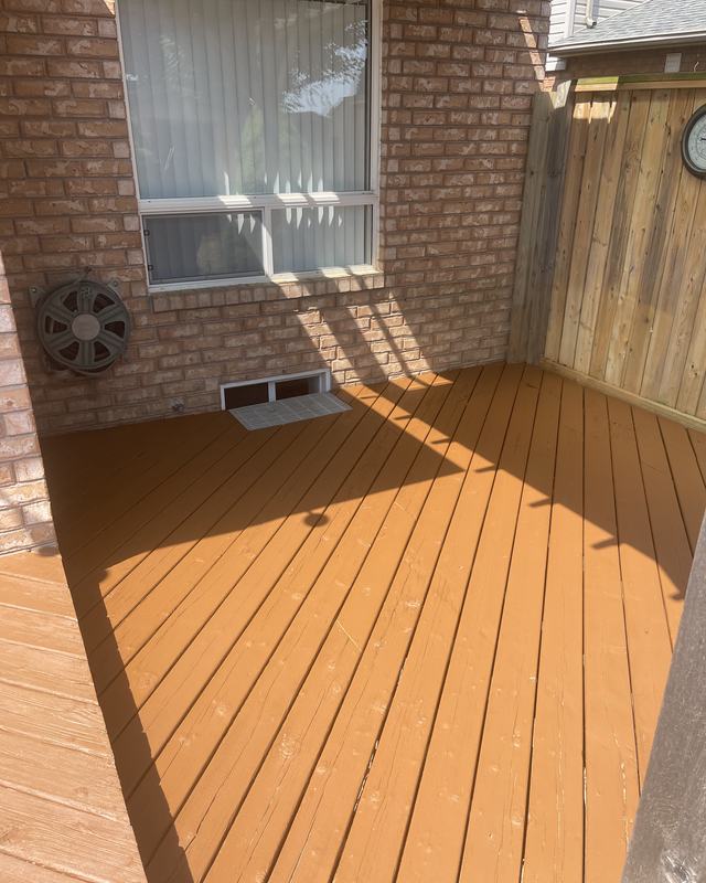 Deck coated in a solid golden cedar stain against a brick wall, cedar privacy screen and outdoor clock