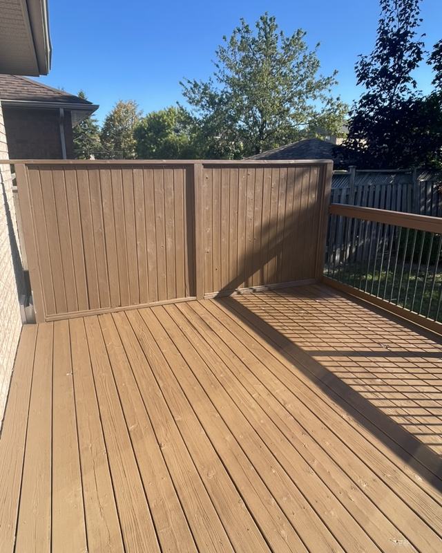 Corner of a stained deck with black spindle railing and a matching cedar privacy screen, open yard behind