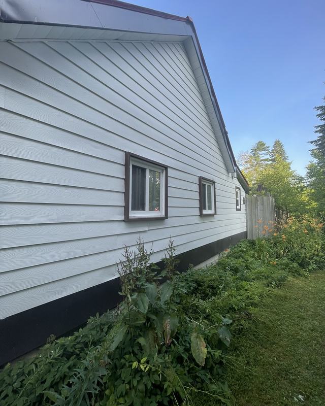 Side of a white-sided home after exterior painting with dark trim detail at the window and foundation line