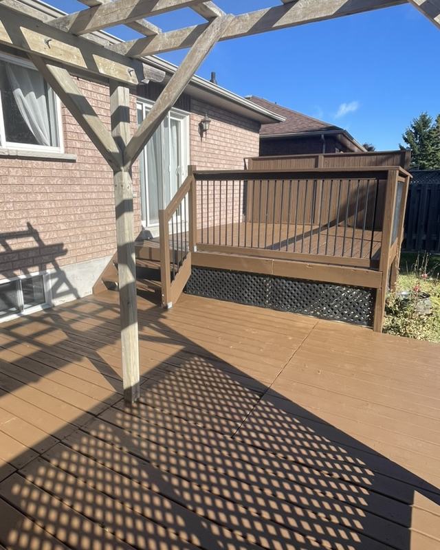 Stained deck beneath a wood pergola casting lattice shadows, brick home and stairs down to the yard