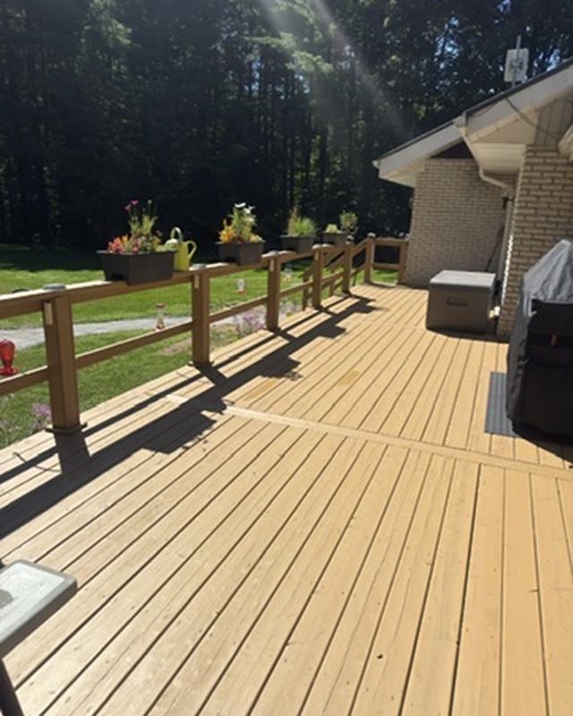 Long deck stained in a light natural tone catching low sun, planters on the railing and a lawn beyond