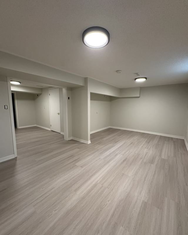 Finished basement rec room painted in a light neutral with pot lights and grey plank flooring