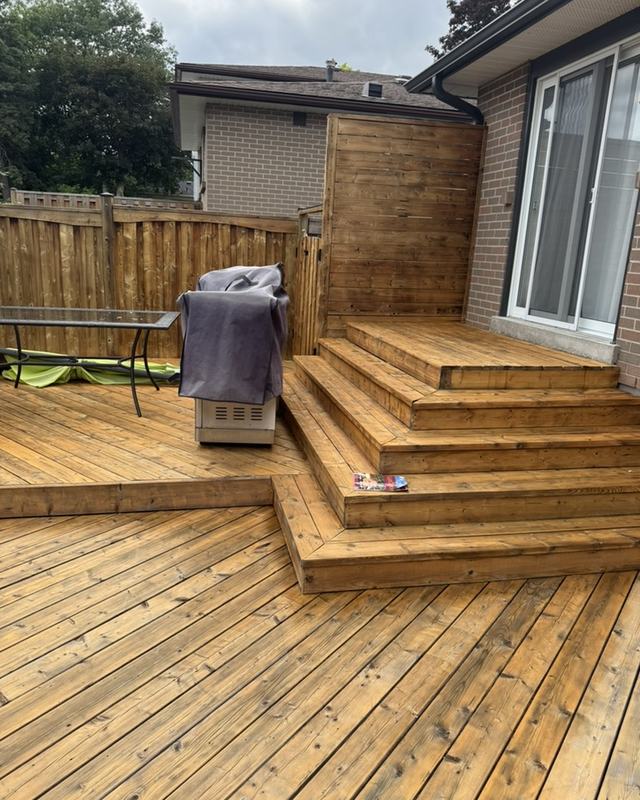 Newly stained deck with wide cascading entry steps in natural wood, board privacy fence to one side