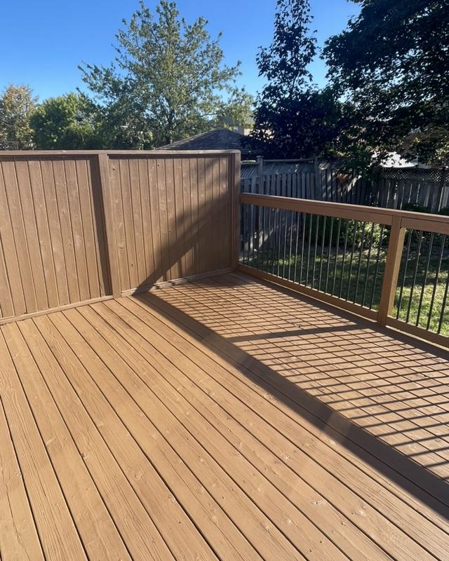 Corner of a stained deck with black spindle railing and cedar privacy panel, open backyard behind