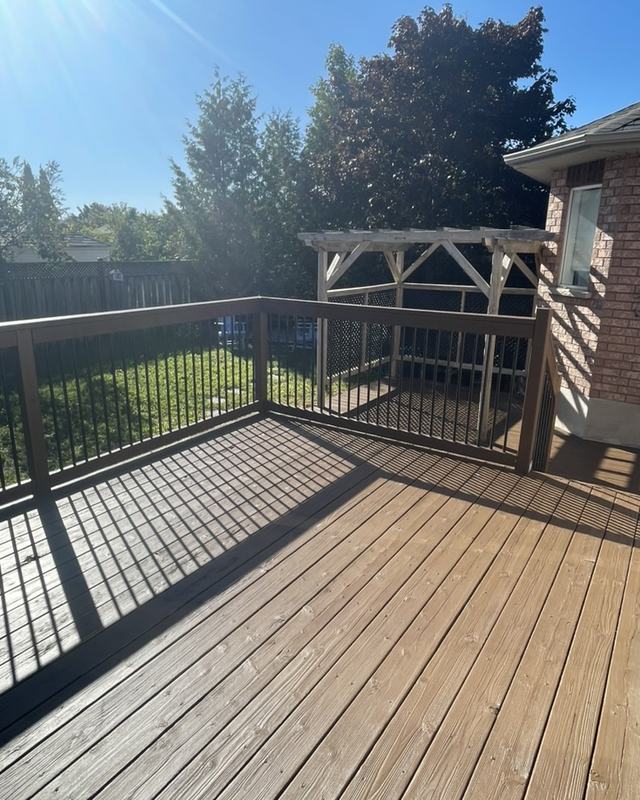 Stained deck with black railing and a wood pergola throwing shade across the boards, open lawn behind