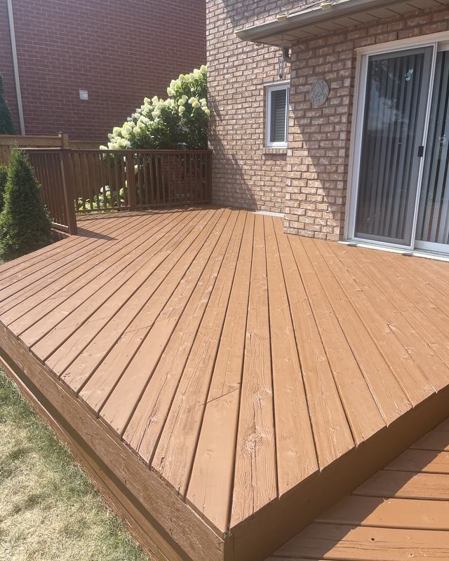 Ground-level deck stained in a cedar tone against a brick home with a sliding patio door and hydrangeas