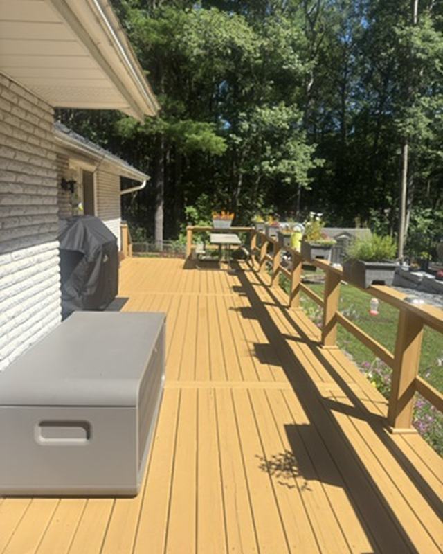 Long deck stained in a golden tone with wood railing, storage bench and a wooded backyard beyond